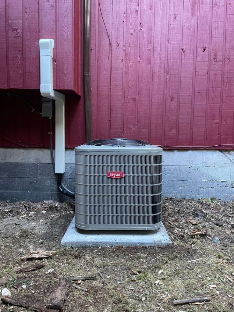 An air conditioner is sitting on the ground in front of a red fence.