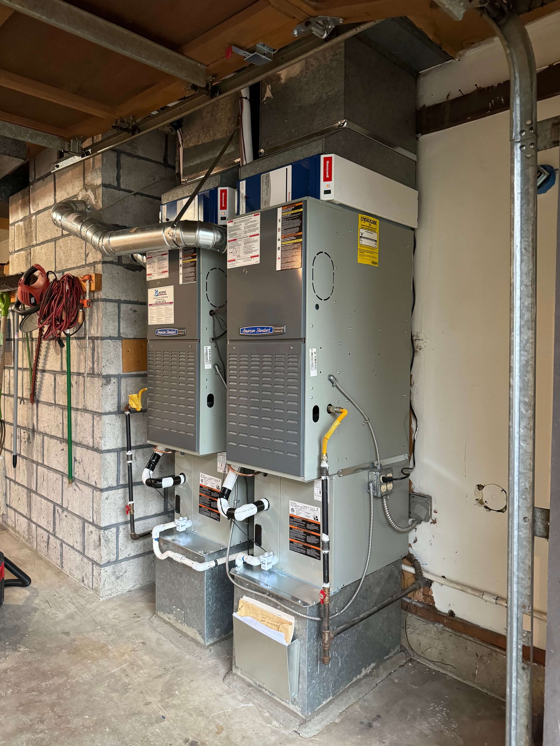 Two air conditioners are sitting next to each other in a garage.